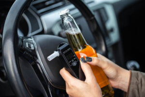 woman with beer bottle and breathalyzer sits in car, implying dangerous drunk driving.