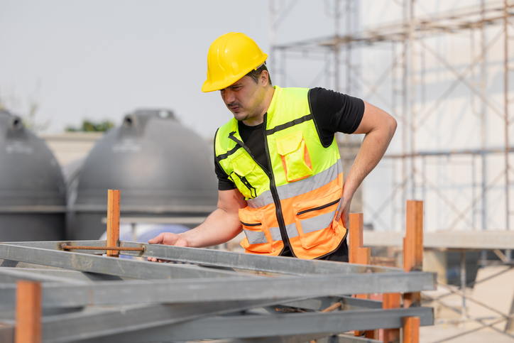 A construction worker in a safety vest and hard hat is focused on tasks at a busy construction site - types of injuries covered by workers’ compensation