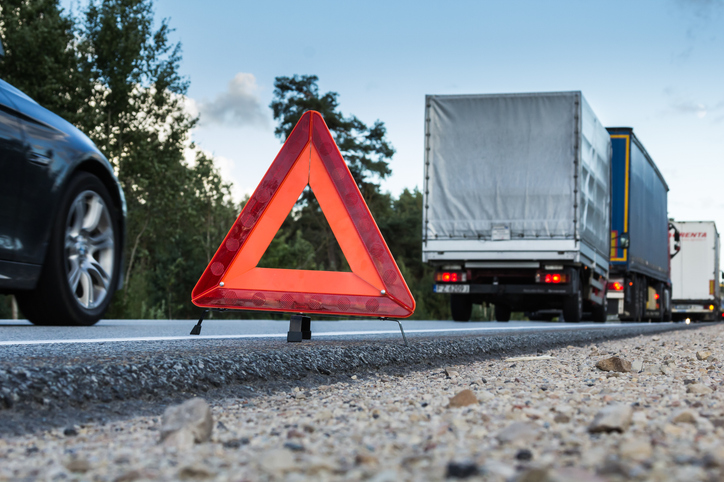 Cars and trucks drive along the road beside a warning sign indicating potential hazards ahead - Why you need a truck accident lawyer