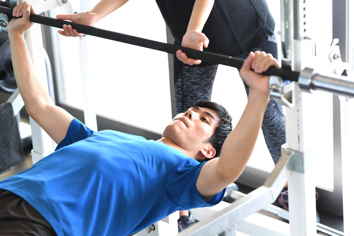 Man and personal trainer assisting doing bench press strength training at the gym - can you sue a personal trainer for injury?