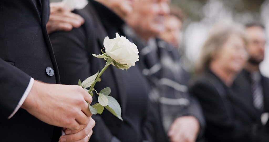 family at funeral with focus on hands and white rose - Honolulu wrongful death lawyer